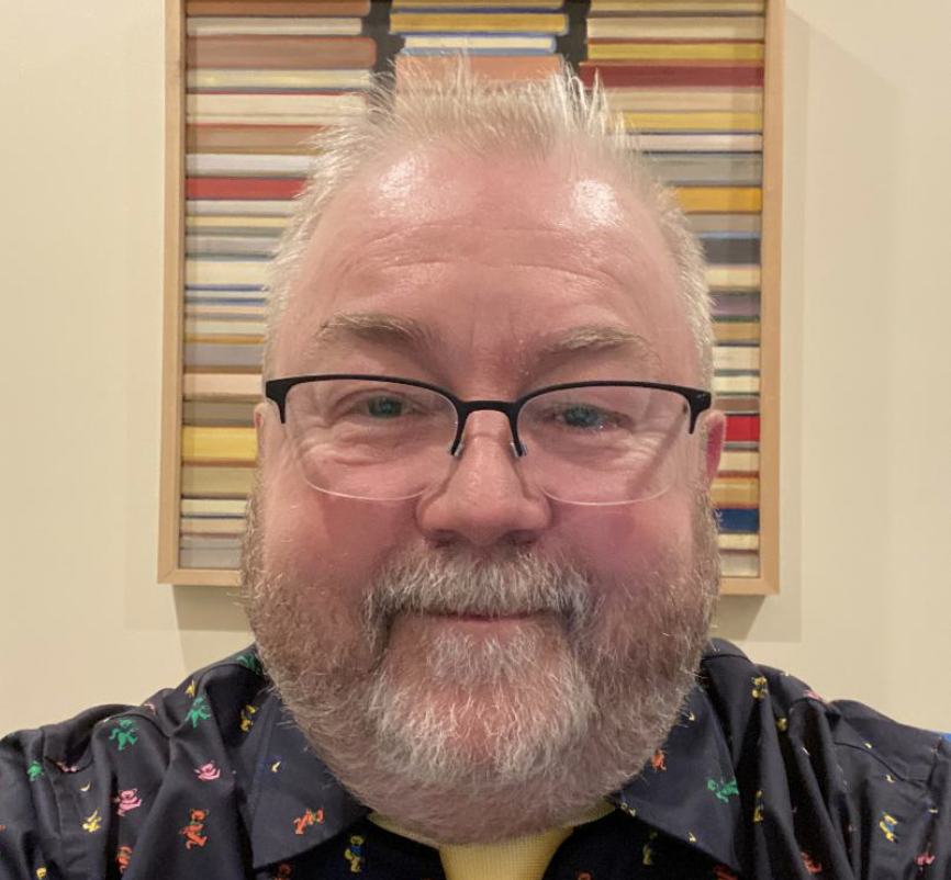 Photo of man (Eric Johnson, MD) with blue collared shirt, white hair and beard, black glasses