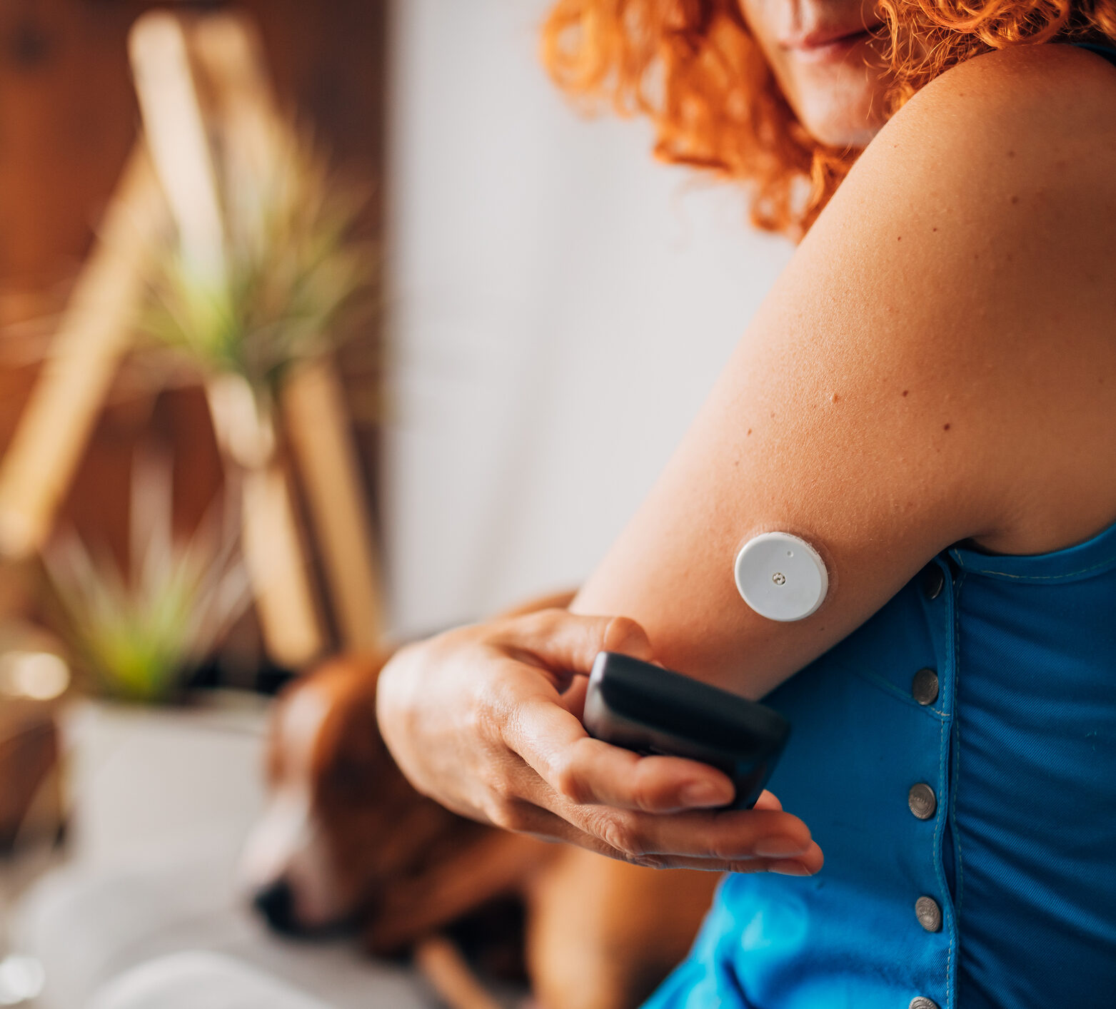 Woman with type 1 diabetes using the continuous glucose monitor reader device, above the glucose blood sensor to scan her blood sugar level