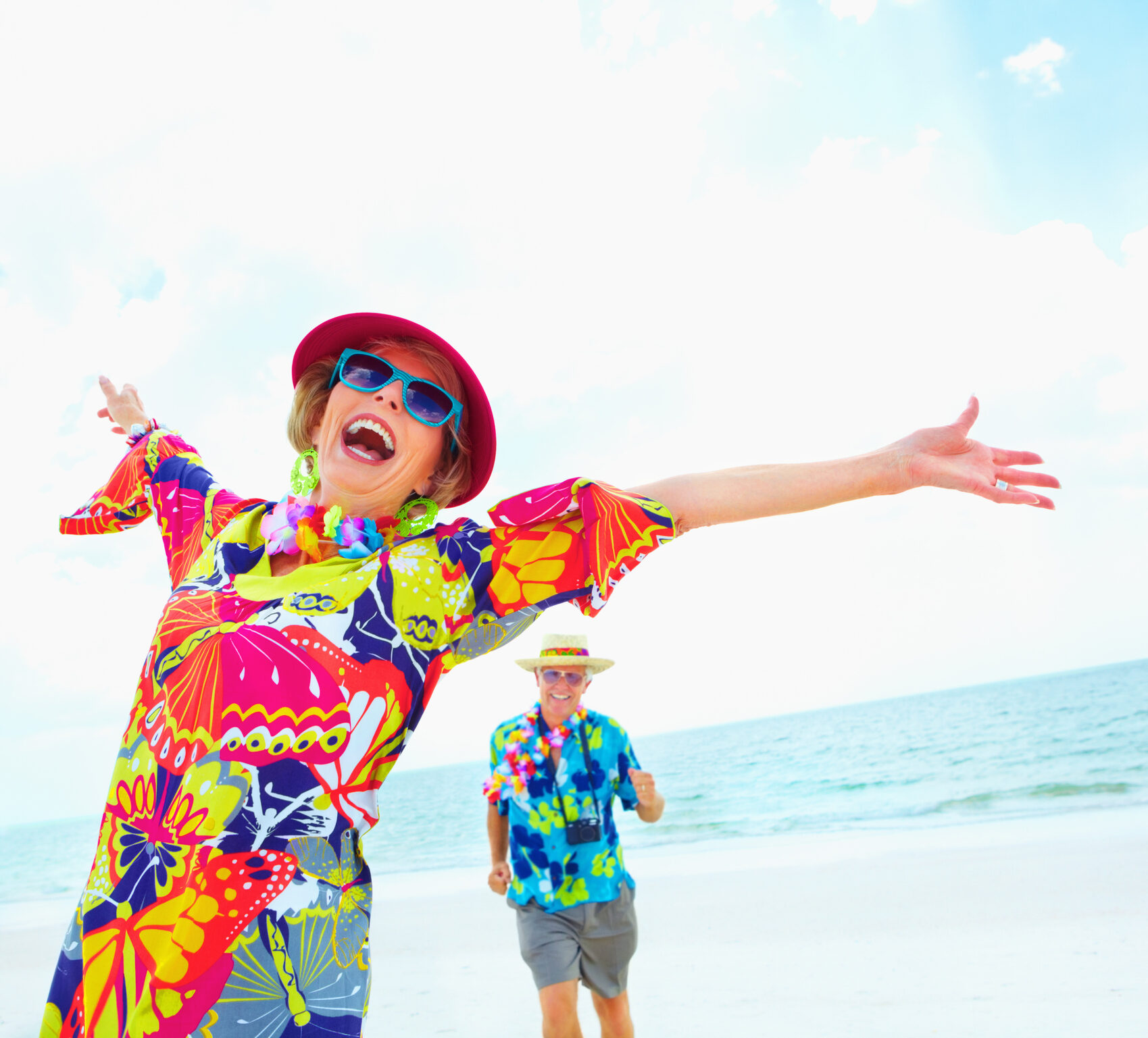 Older woman in brightly colored outfit on the beach with her arms thrown back