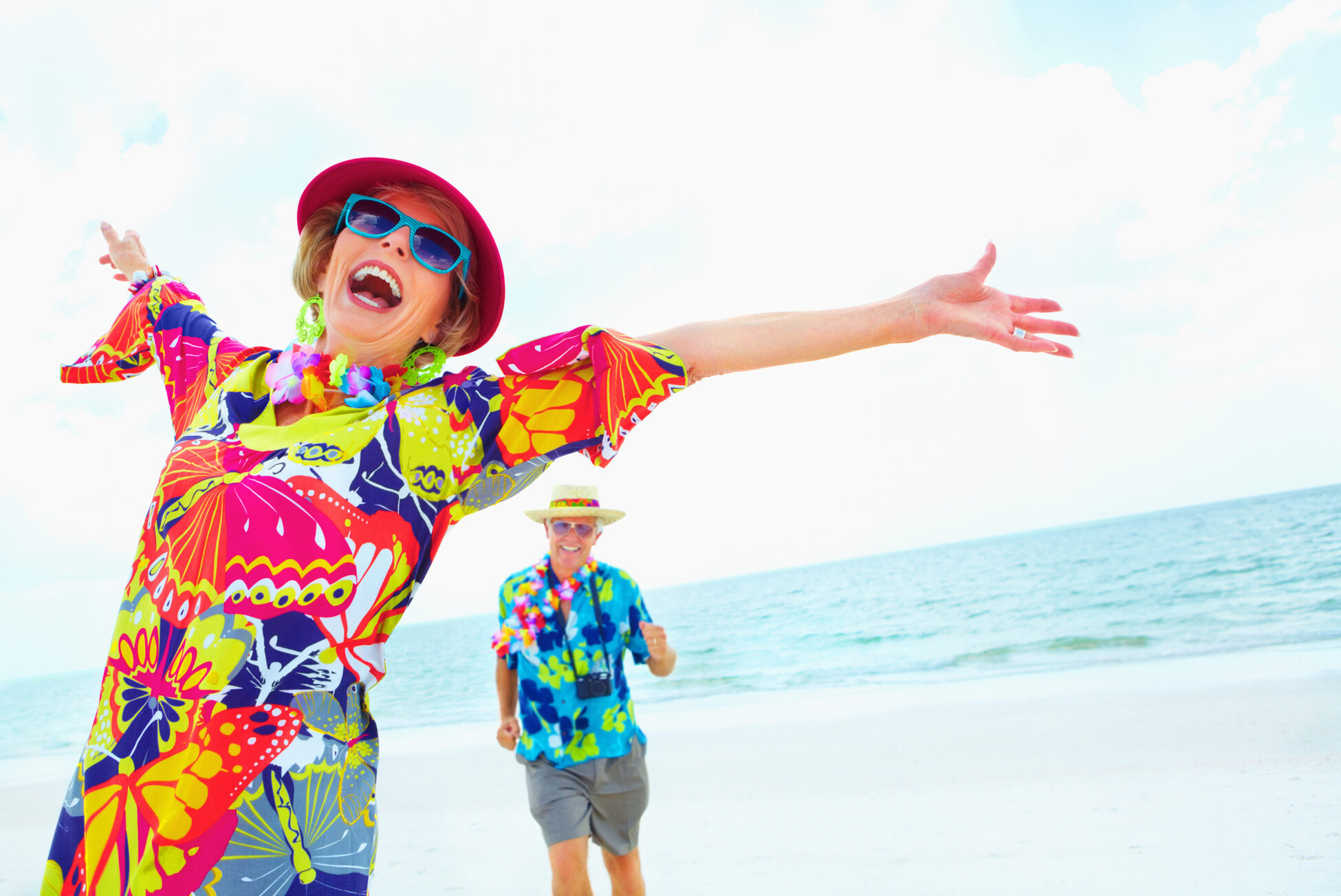 Older woman in brightly colored outfit on the beach with her arms thrown back