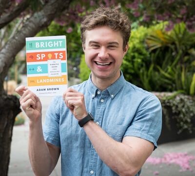 Young man holding a book he wrote smiling, 42 factors that affect time in range, blood glucose