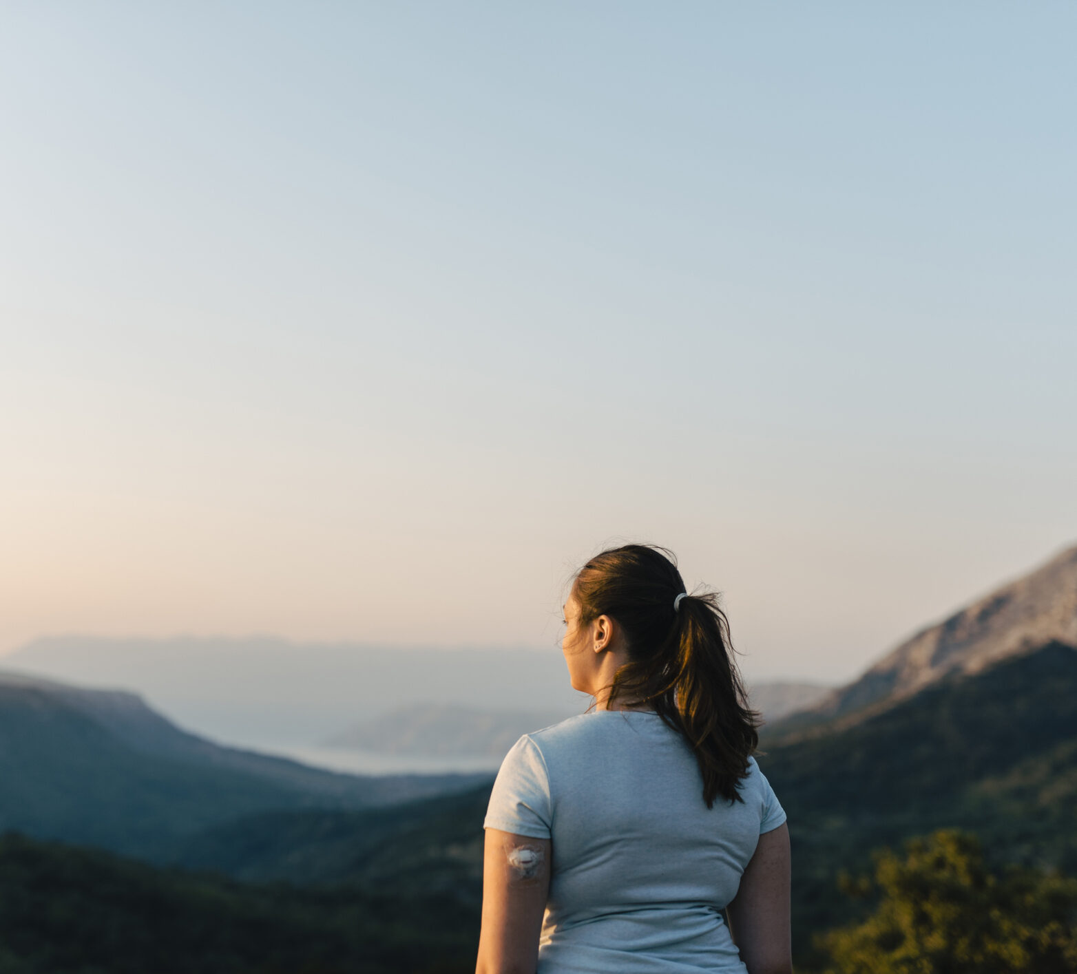 Woman wearing a CGM on a hike looking out at a mountain view