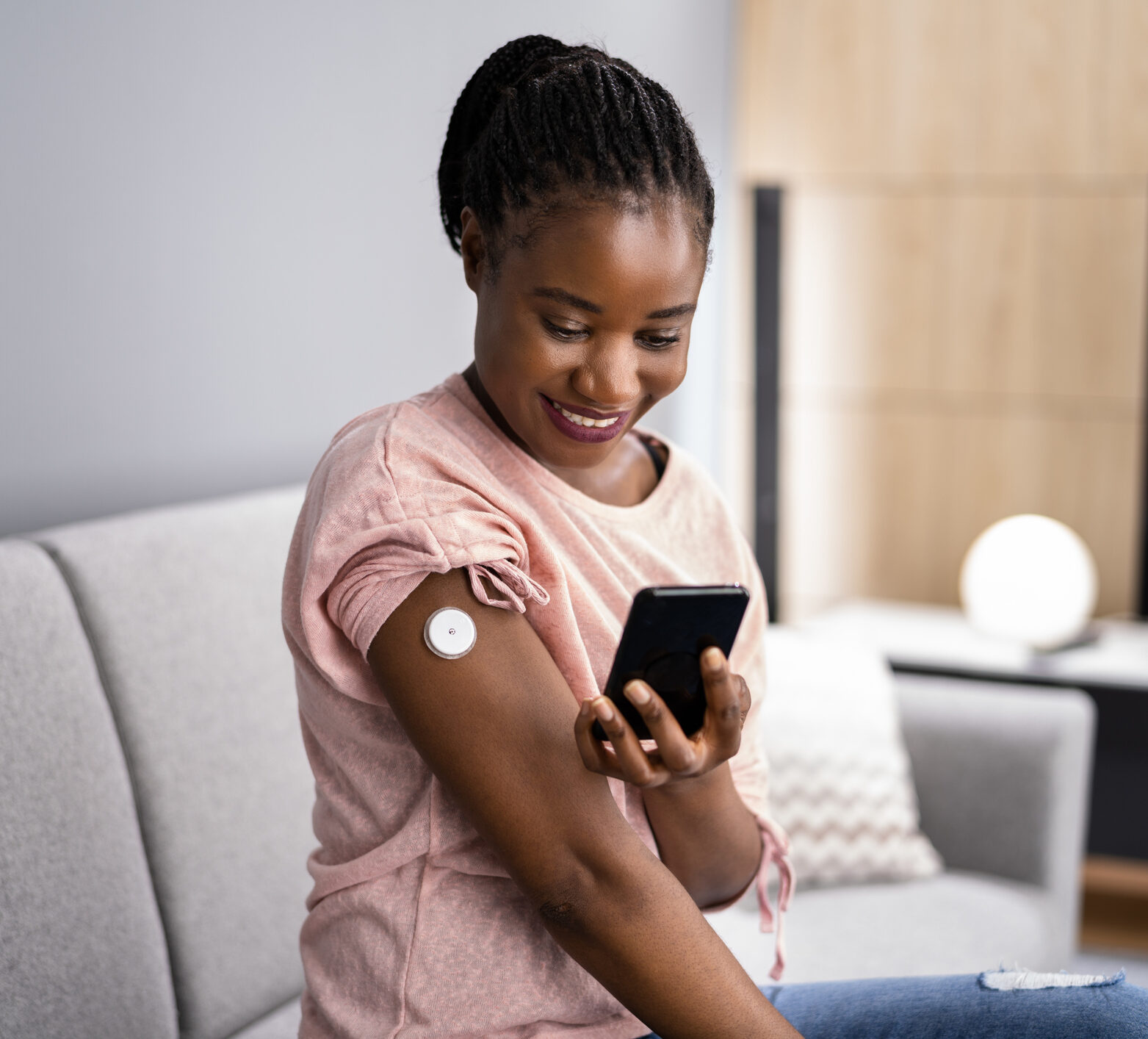 Woman wearing a CGM looking at her time in range on her phone and smiling