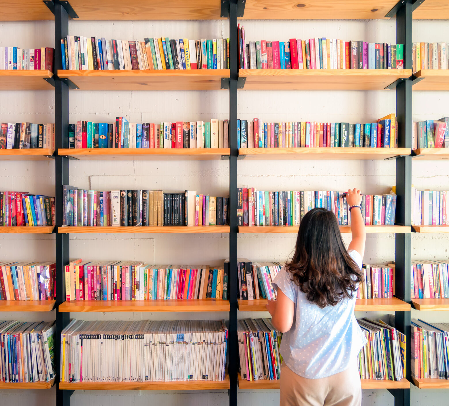A woman looking up at a big bookshelf of colorful books, time in range education and resources