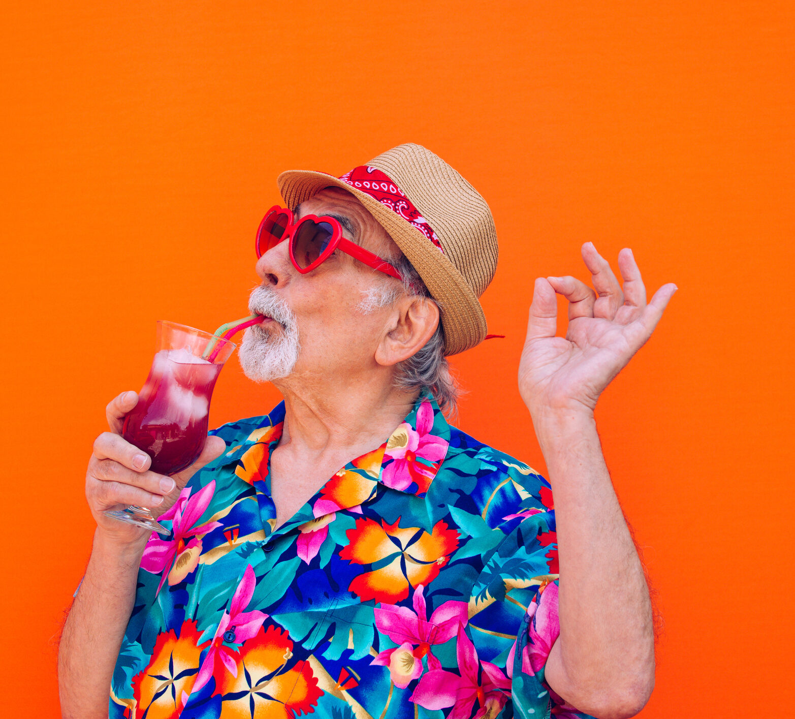 Senior man in a floral shirt drinking a tropical drink, living his best life