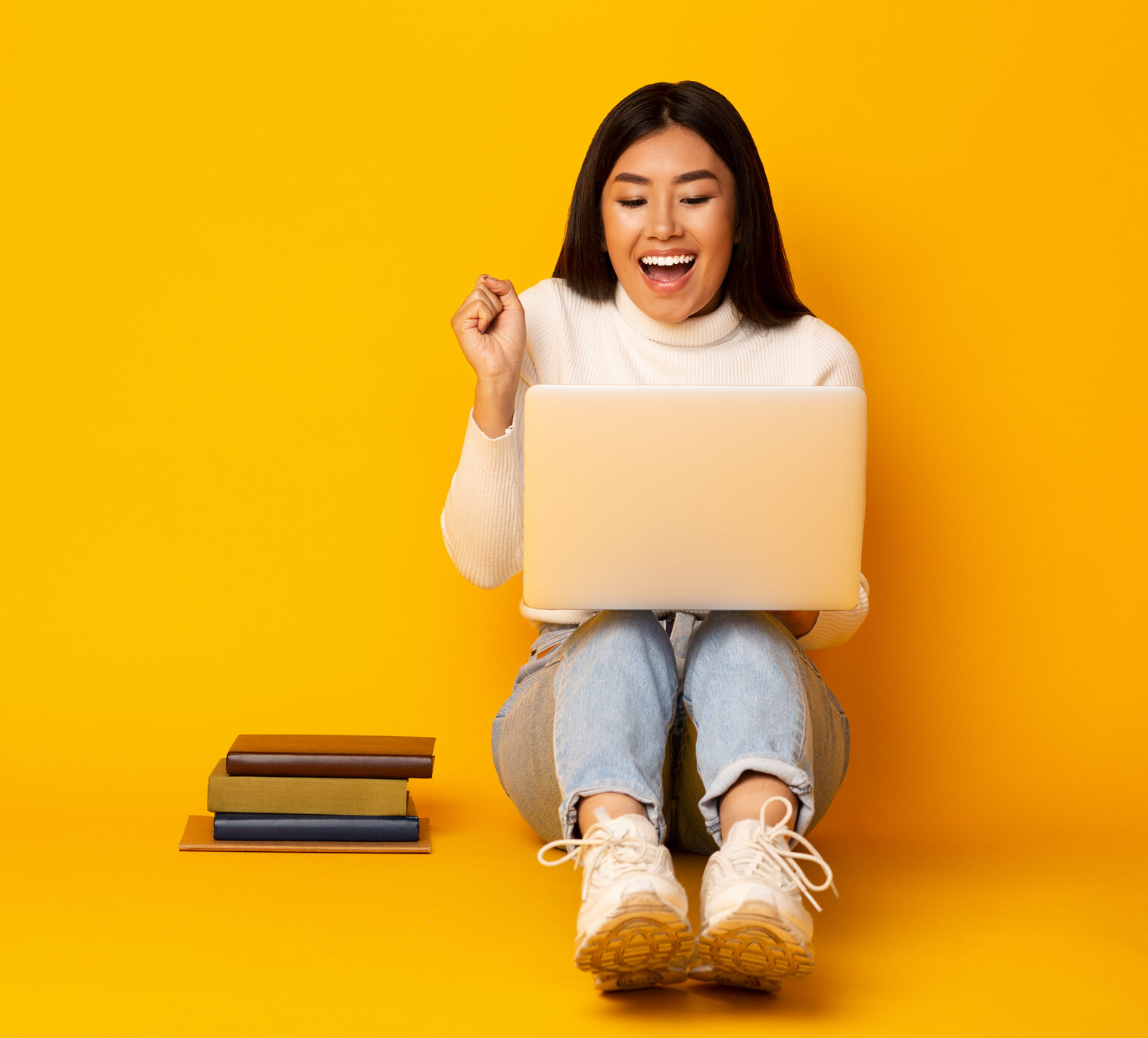 Woman sitting down with a laptop excited, yellow background behind her—meant to convey excitement about time in range news