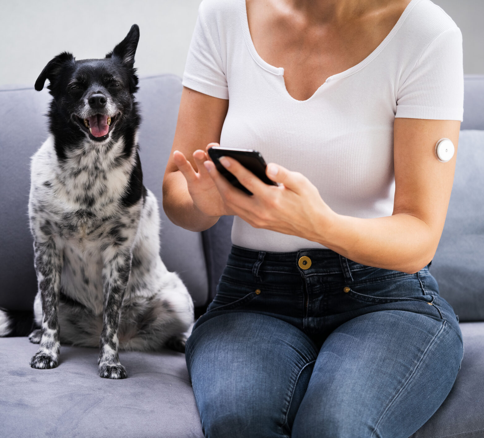 Woman with CGM on her arm checking her time in range on her phone next to her dog
