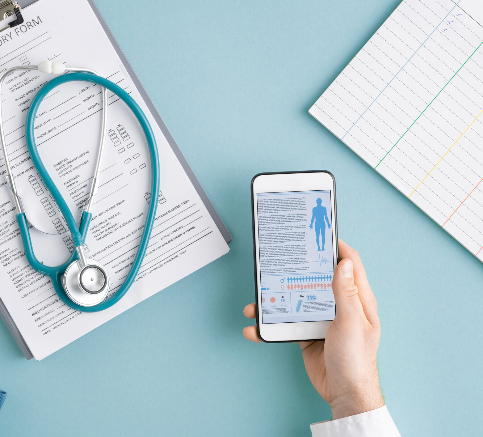 Above view of hands of clinician with gadgets scrolling through medical statistics among document in clipboard with stethoscope and blank card