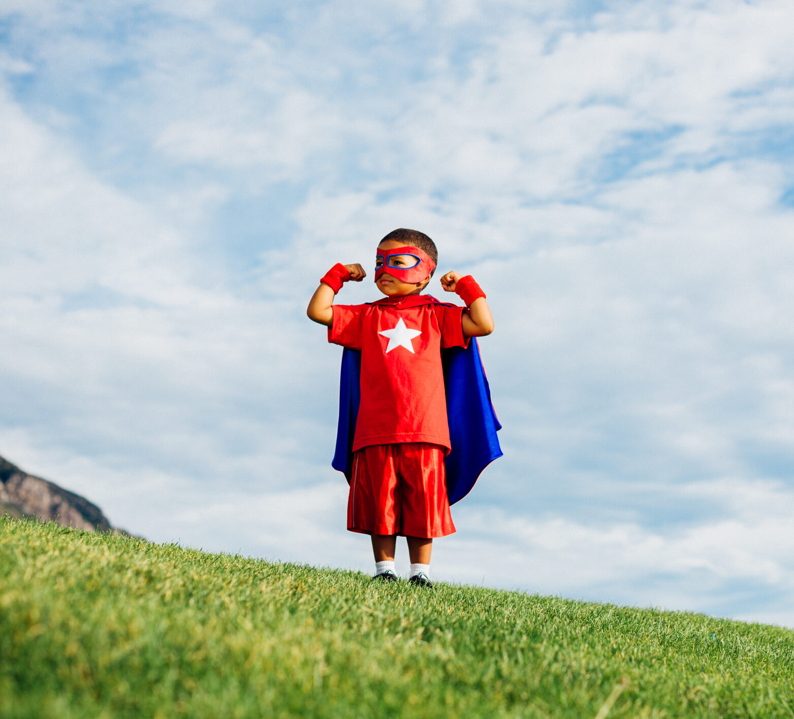A young boy dressed as a superhero with mask and cape with his fists raised in the hair—he's ready for a time in range action plan!