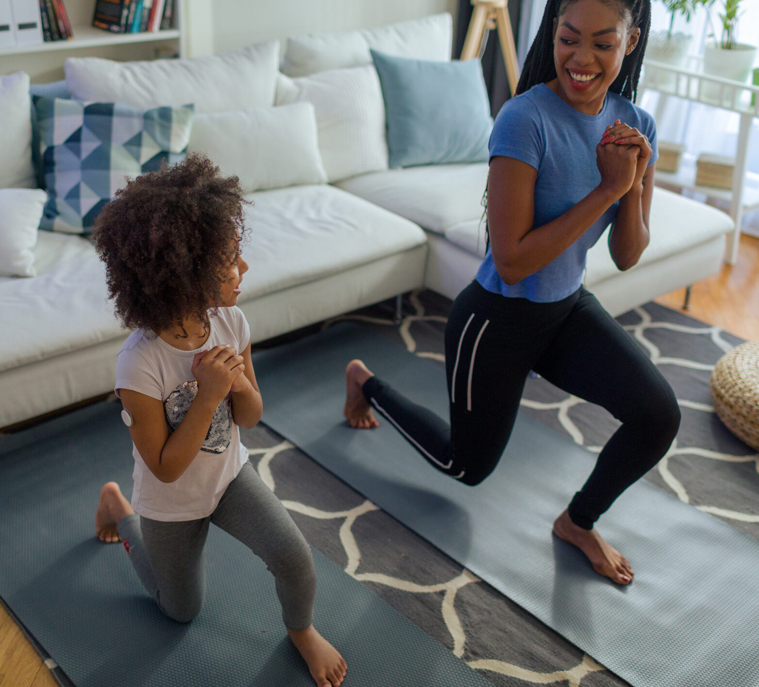 Mother and daughter exercising at home. Cute girl has continuous glucose monitor on her arm.