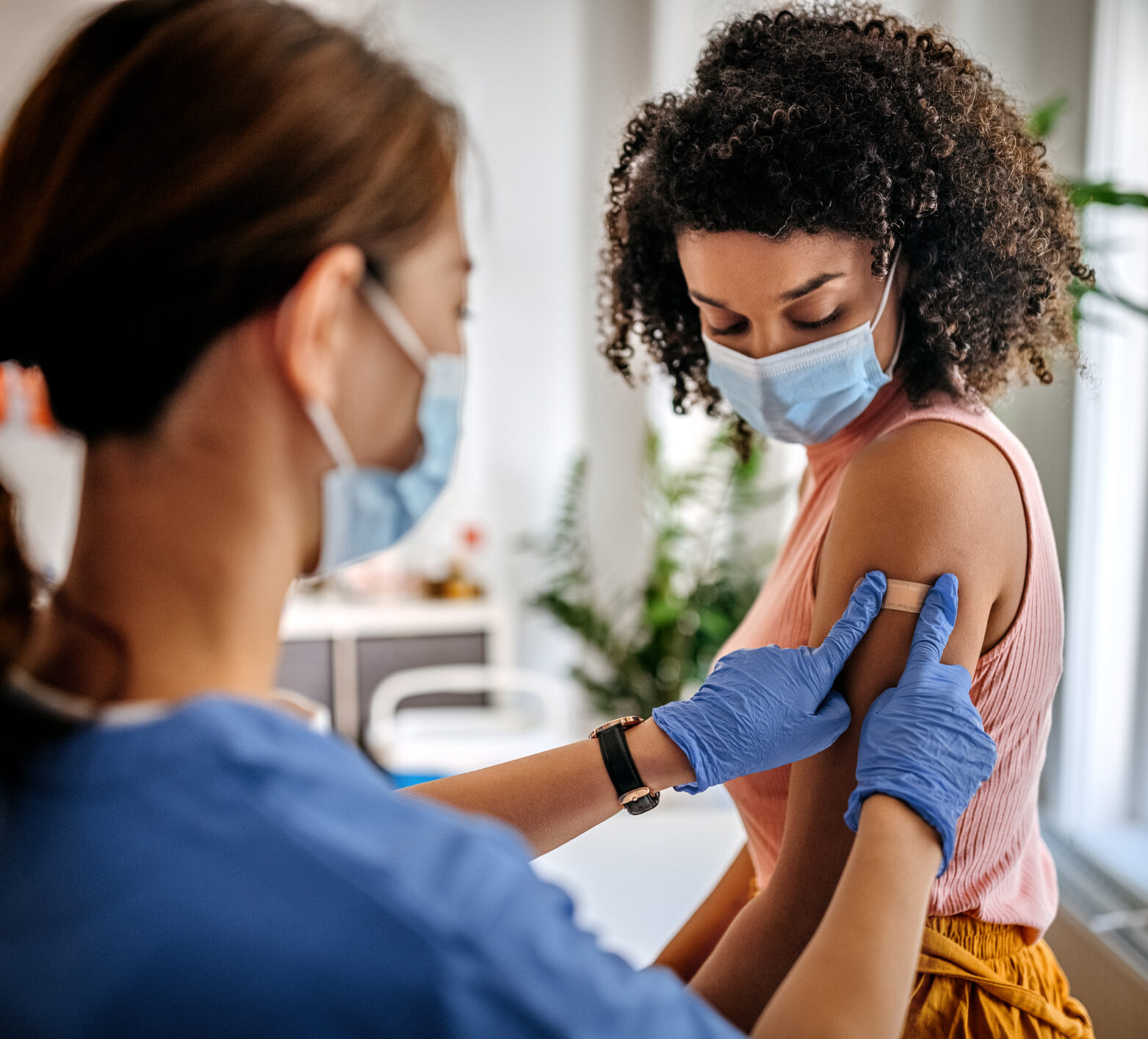 Photo of nurse putting adhesive bandage on young woman patient’s arm after vaccination at a clinic.