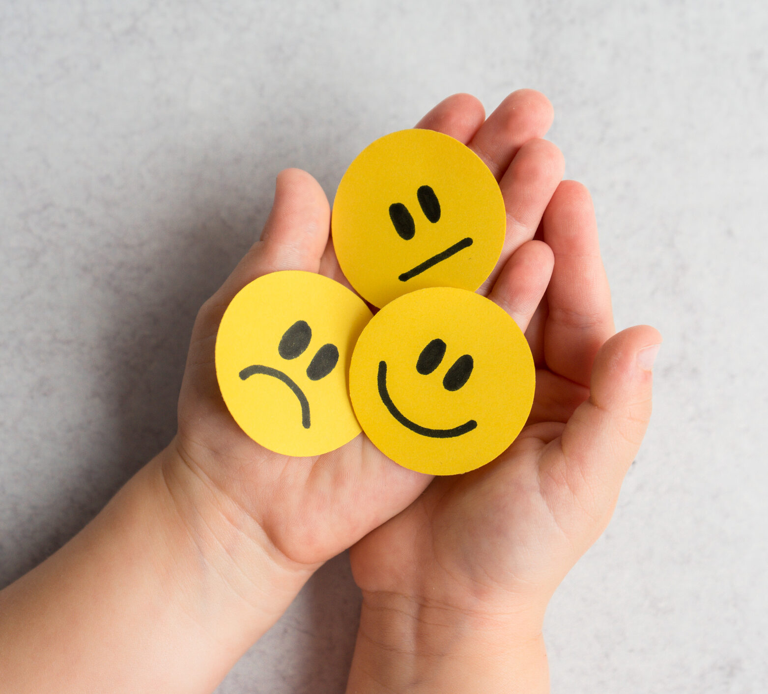 Kid’s hands holding happy, sad and unsatisfied paper faces, meant to show the different moods that come with living with diabetes