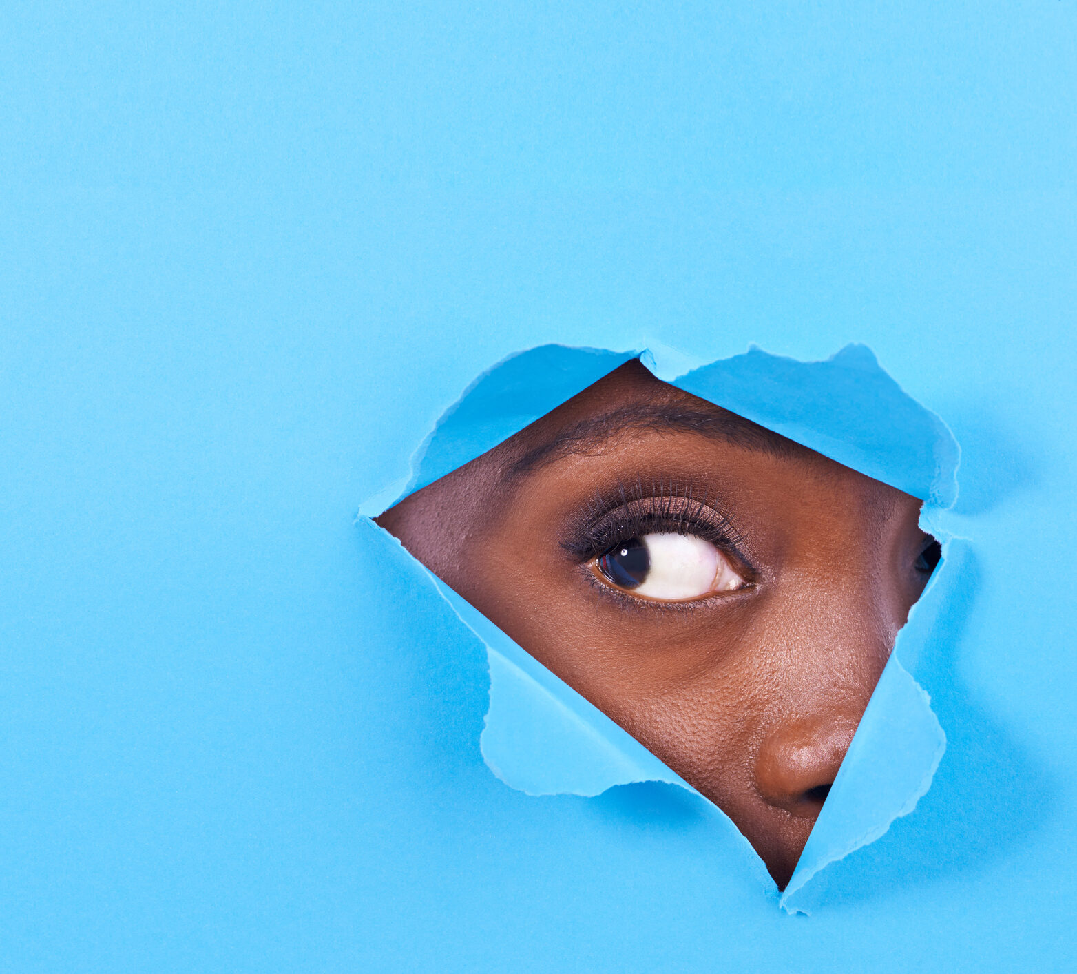 Woman's eye peeking through torn blue paper
