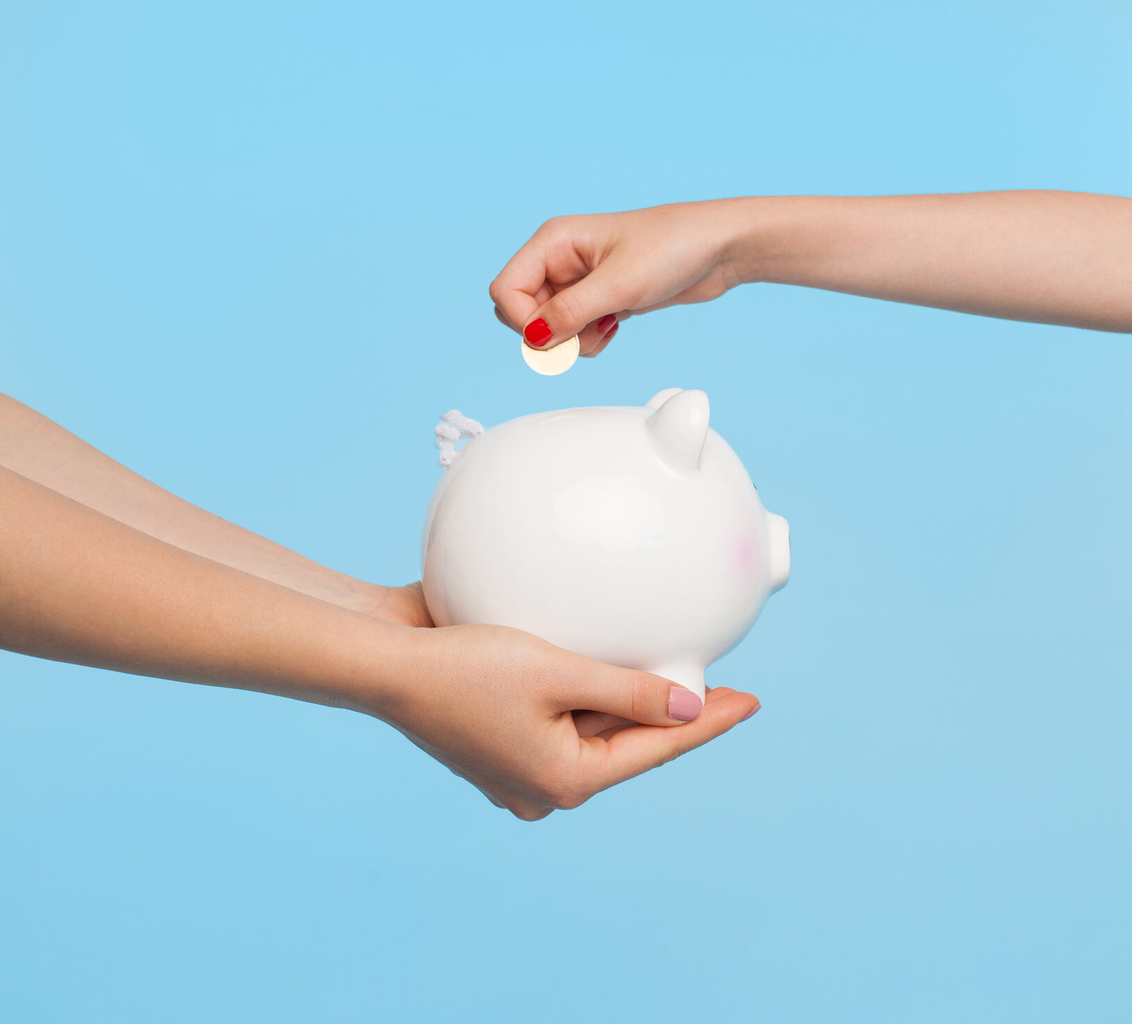 Side view of female hands holding white piggy bank and shining coin against blue background—meant to convey CGM affordability cost savings programs